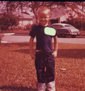 Kirk Rogers prepares for his first day of Kindergarten outside his house. The giant name tag has his name and address. 1959. 